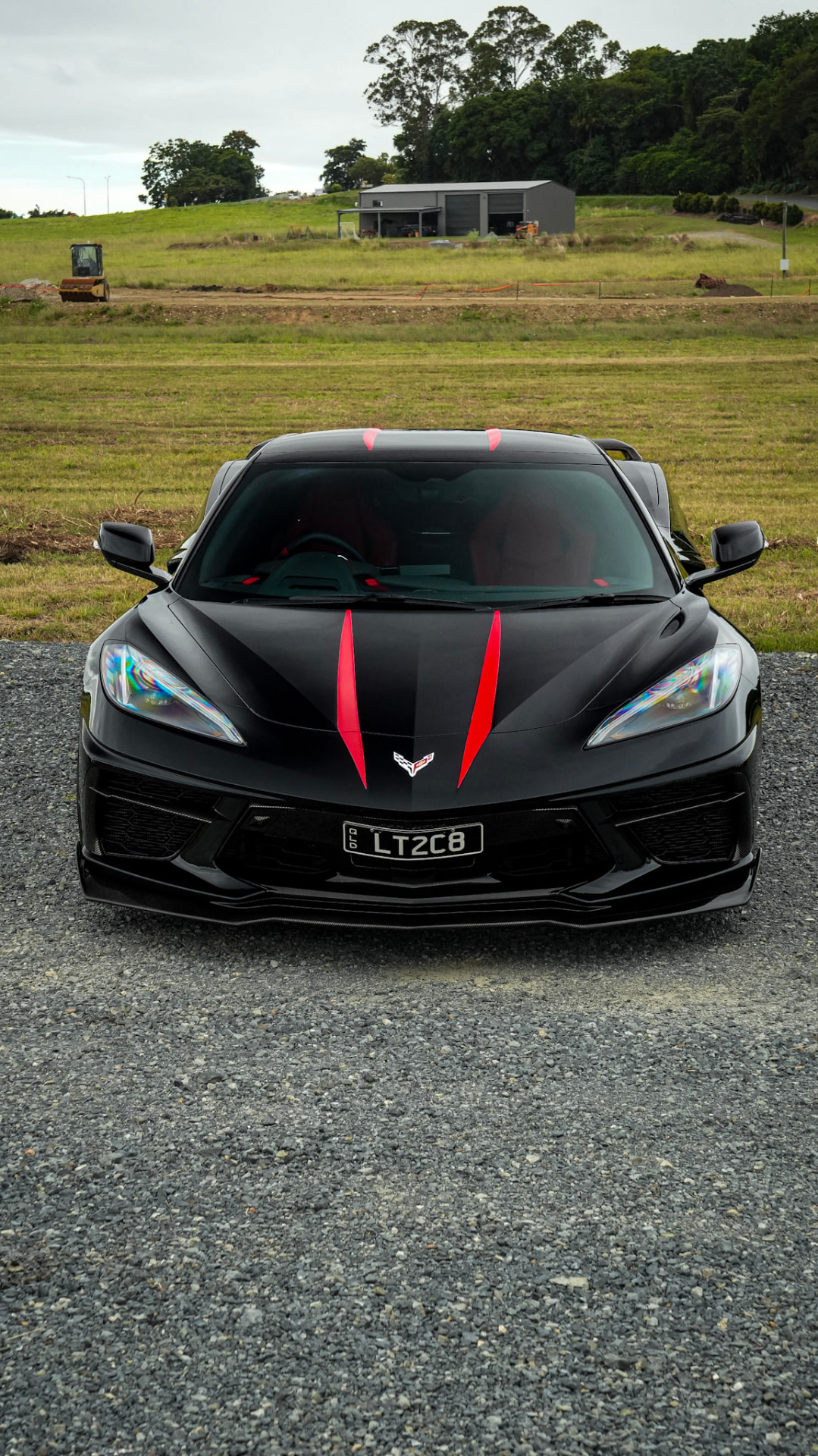 Corvette C8 head-on on gravel with green paddocks behind