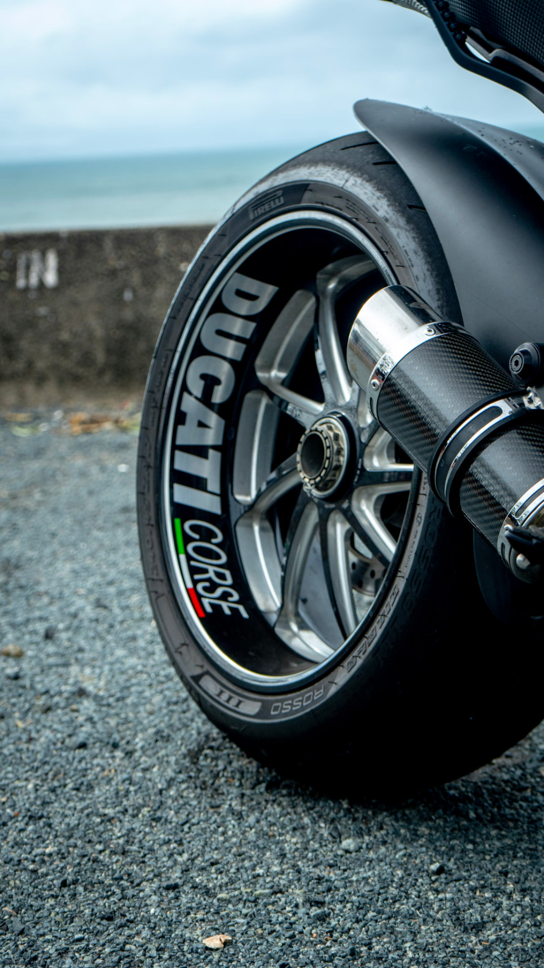 Ducati Diavel rear wheel and carbon exhaust with the ocean behind